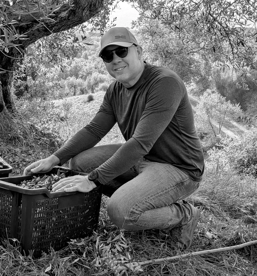 Ernesto Crucet kneeling beside a crate of freshly picked olives in an olive grove in Umbria.